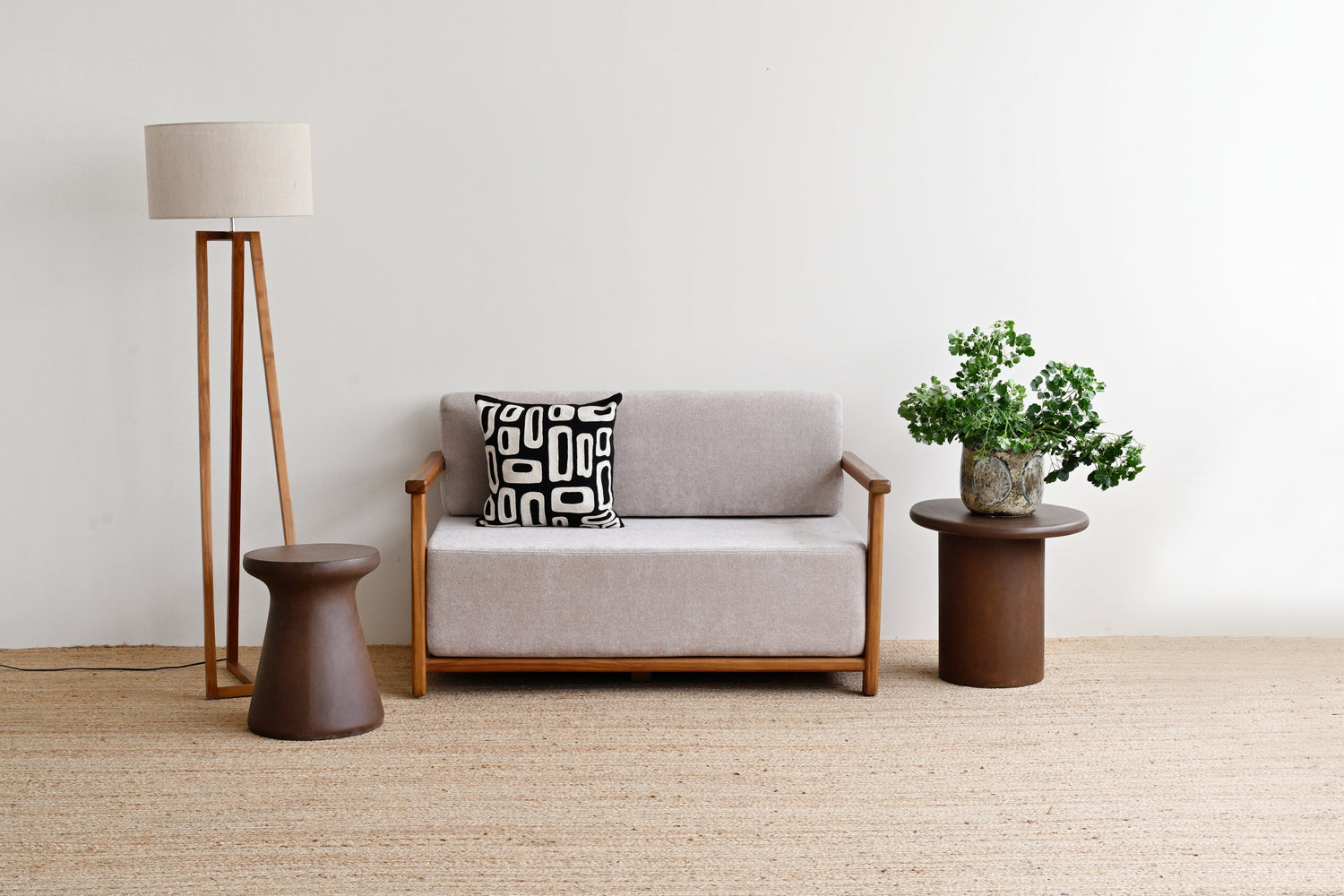 Gray sofa with a patterned pillow, standing lamp, and small table with a plant in a minimalistic room.