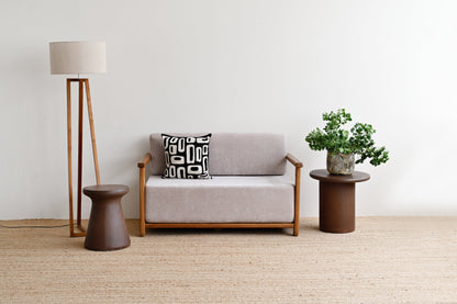 Gray sofa with a patterned pillow, standing lamp, and small table with a plant in a minimalistic room.