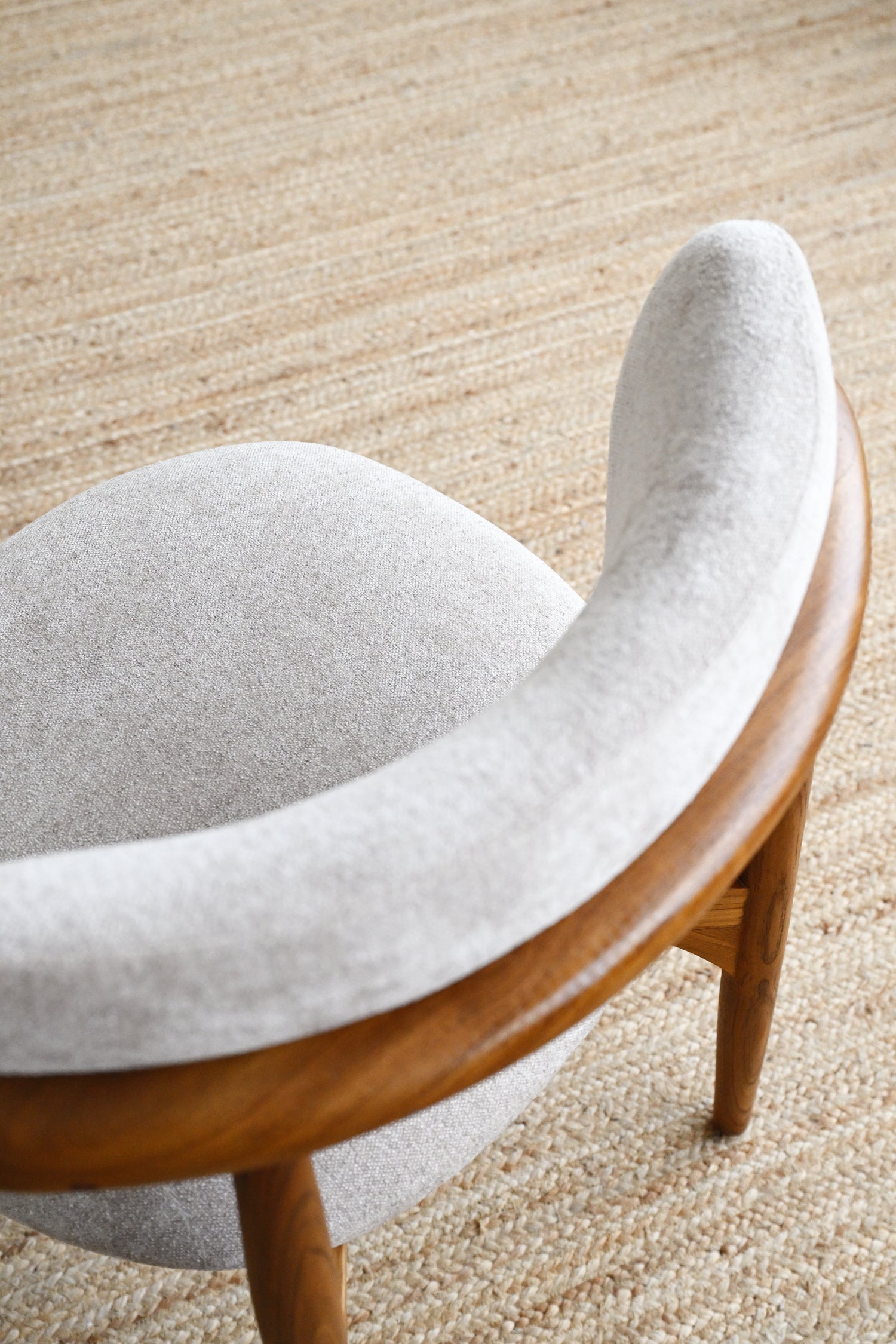 Curved chair with wooden frame and gray cushion on a beige carpet