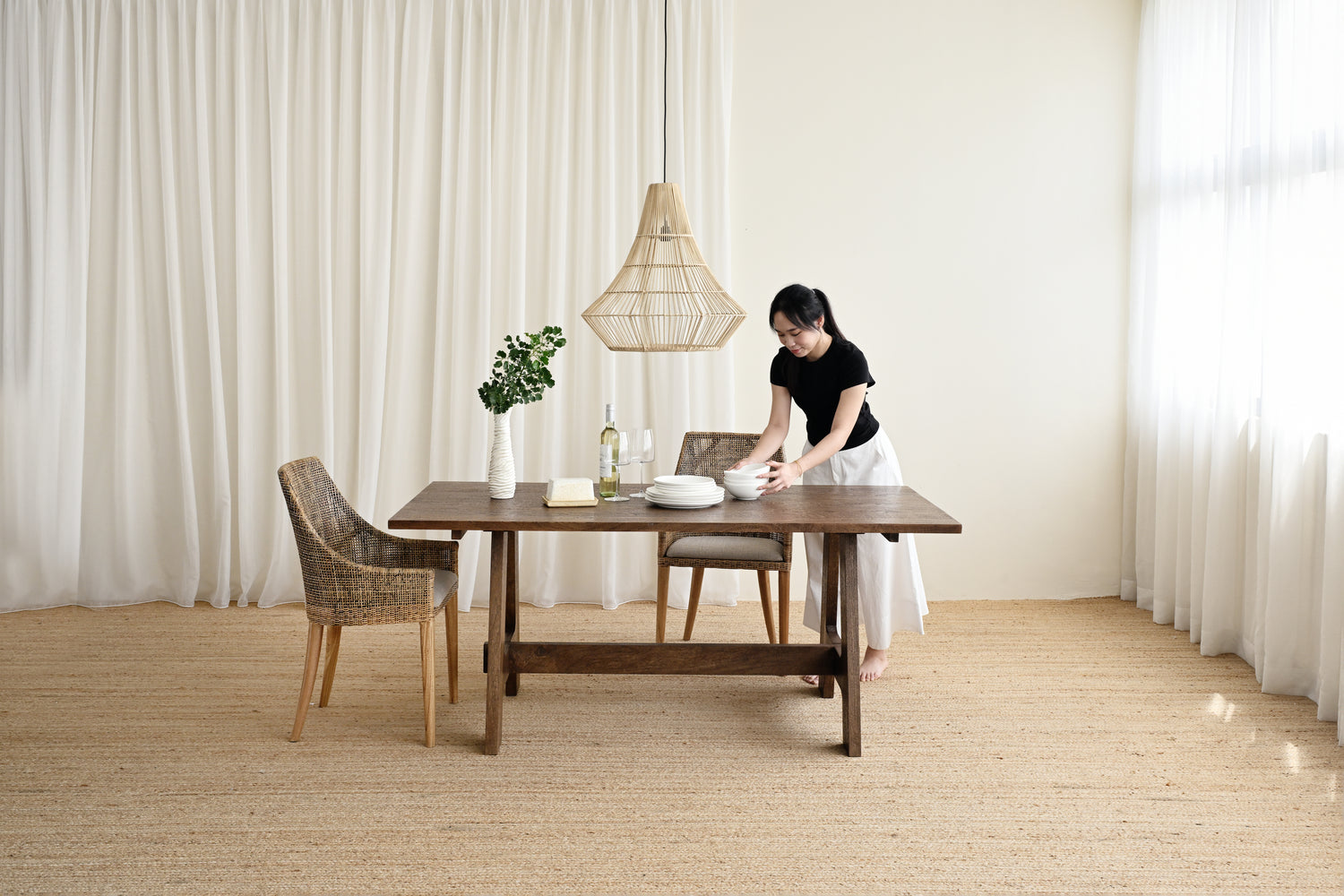 Woman setting a table in a room with large windows and neutral decor