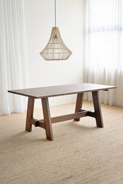 Wooden dining table with a hanging light fixture in a room with white curtains and beige carpet.