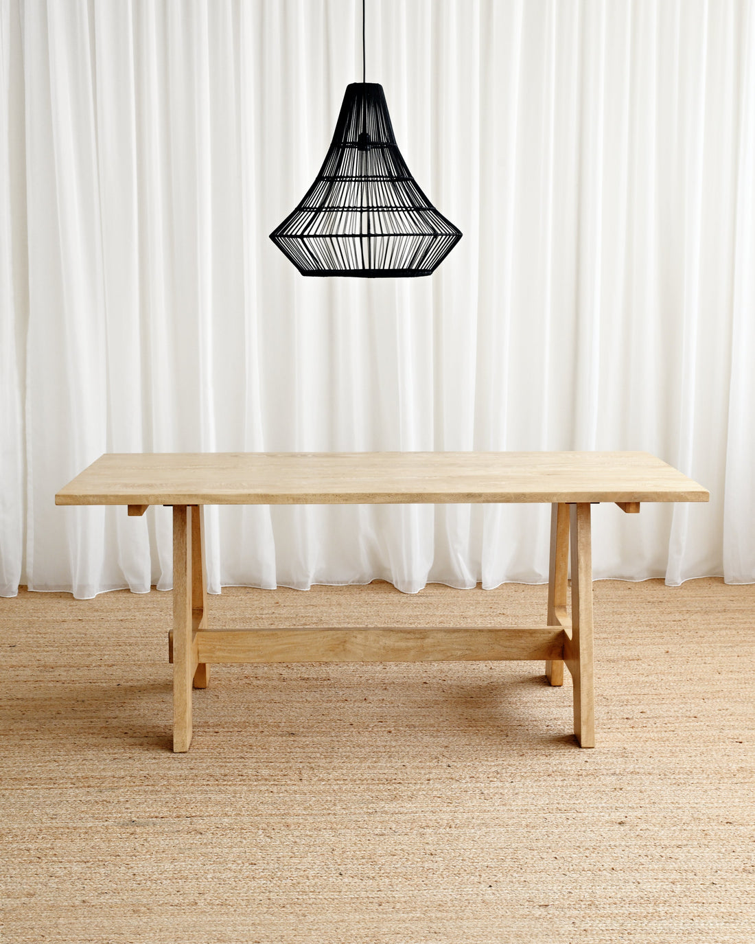 Wooden table with a black pendant light against a white curtain background