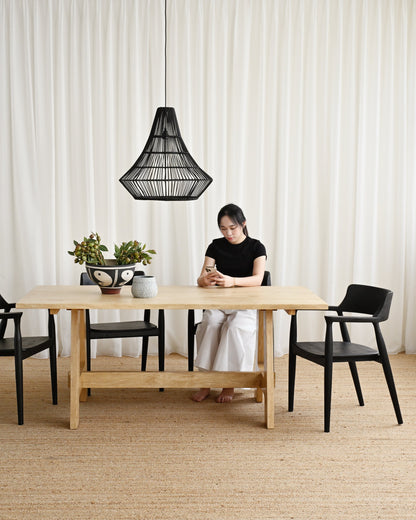 Person sitting at a wooden table with black chairs in a room with white curtains.