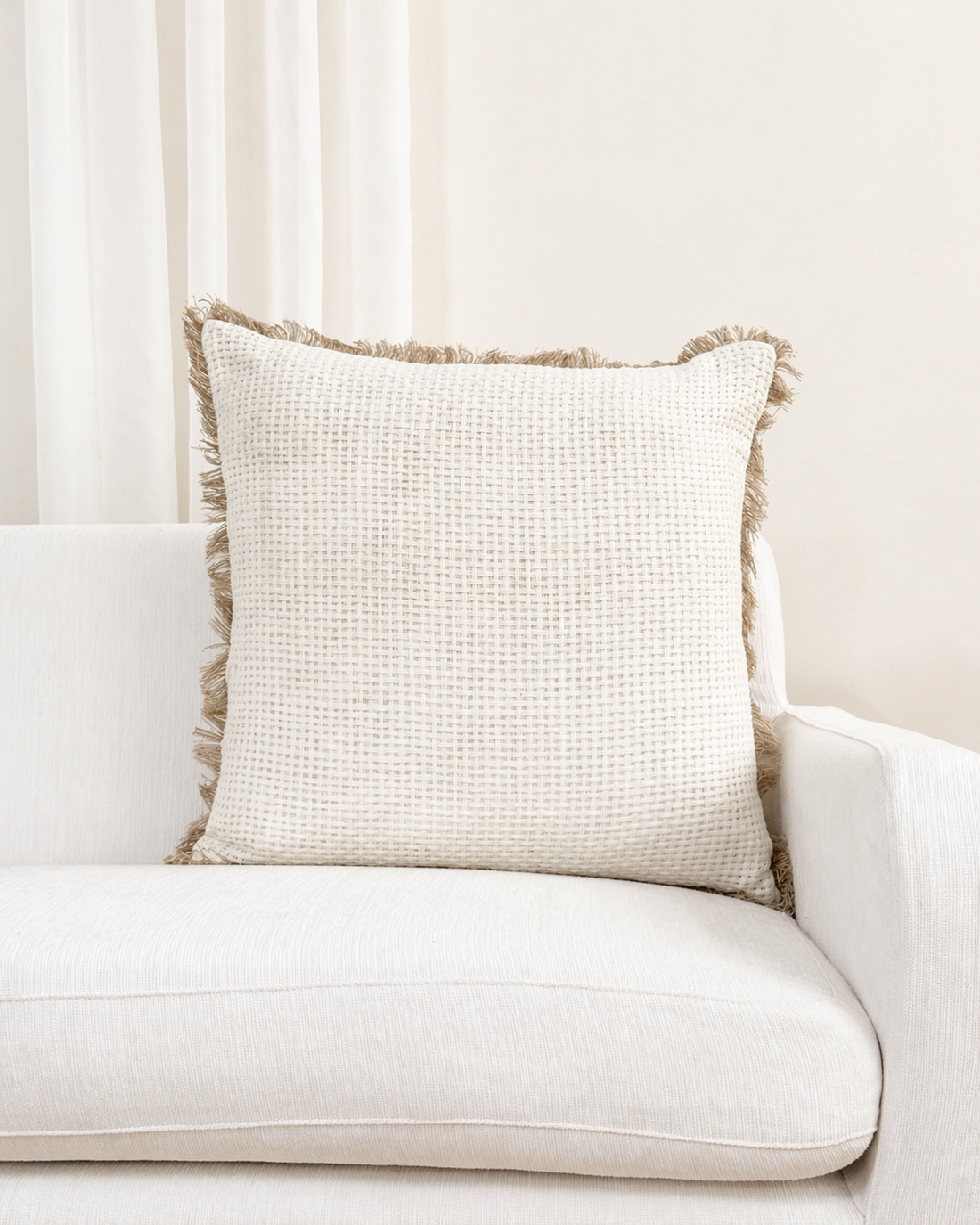 Beige pillow with textured trim on a white sofa against a neutral wall.