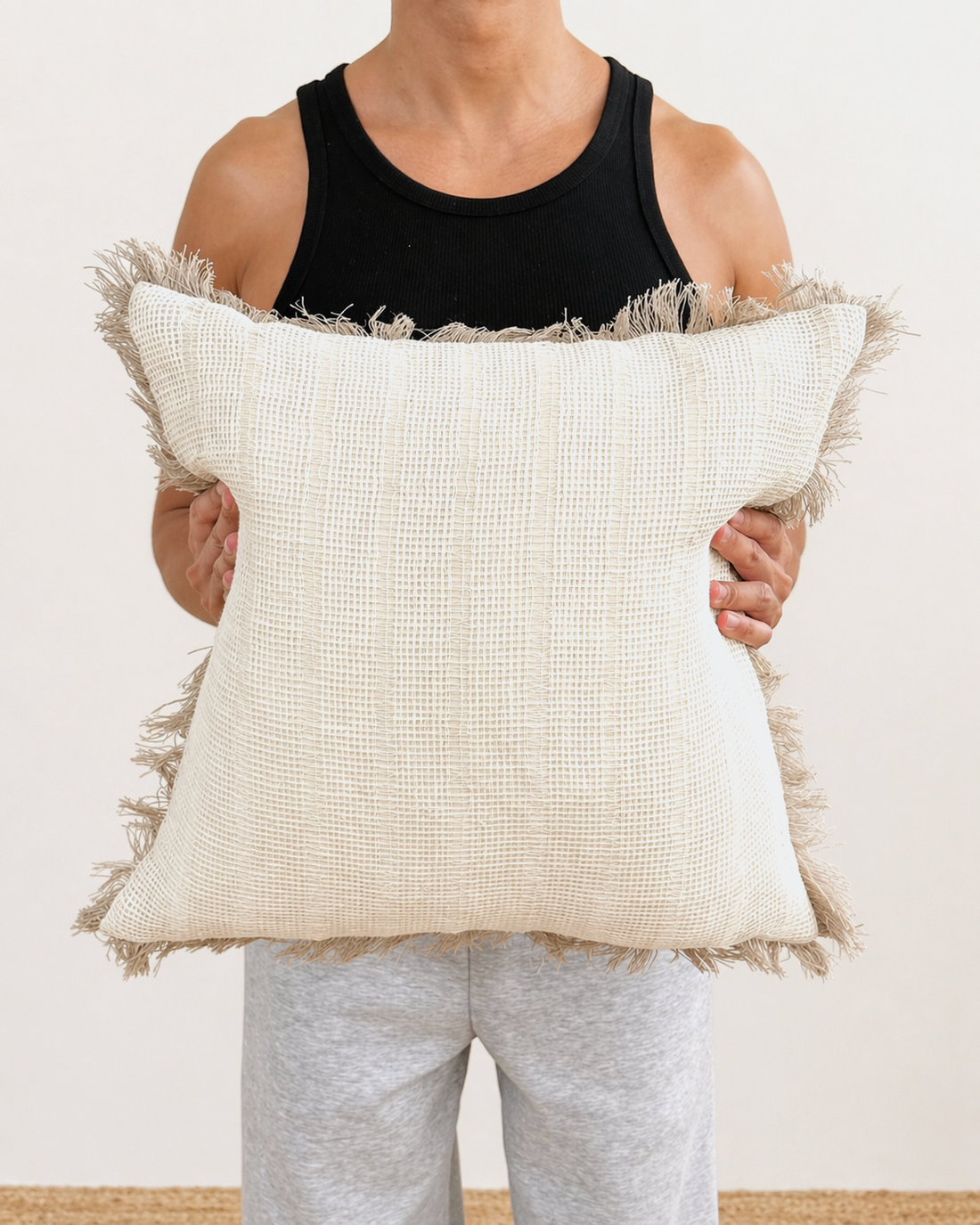 Person holding a large decorative pillow with a textured pattern and frayed edges.