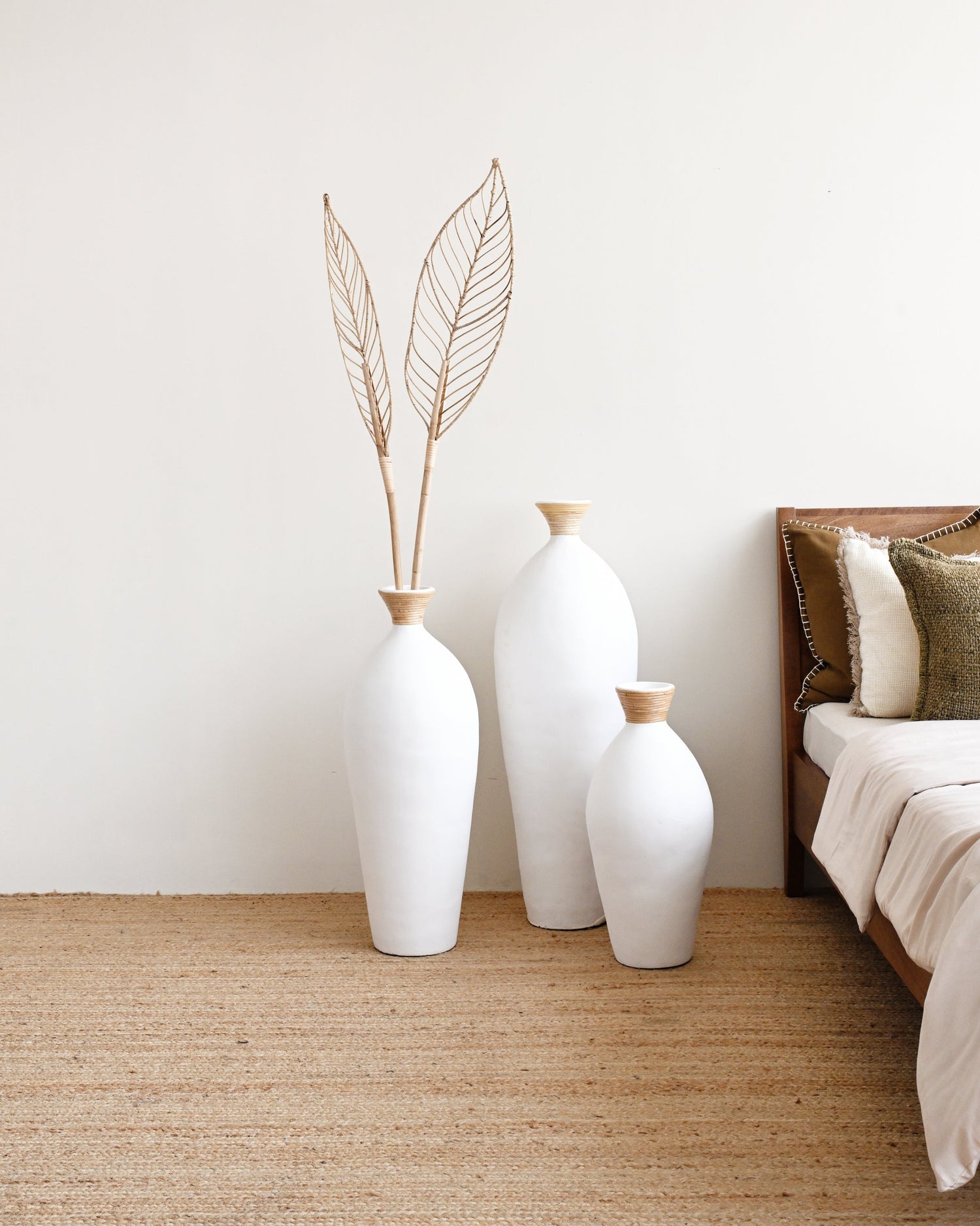 Three white vases with gold accents on a beige rug next to a bed.