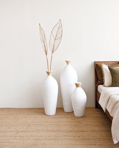 Three white vases with gold accents on a beige rug next to a bed.