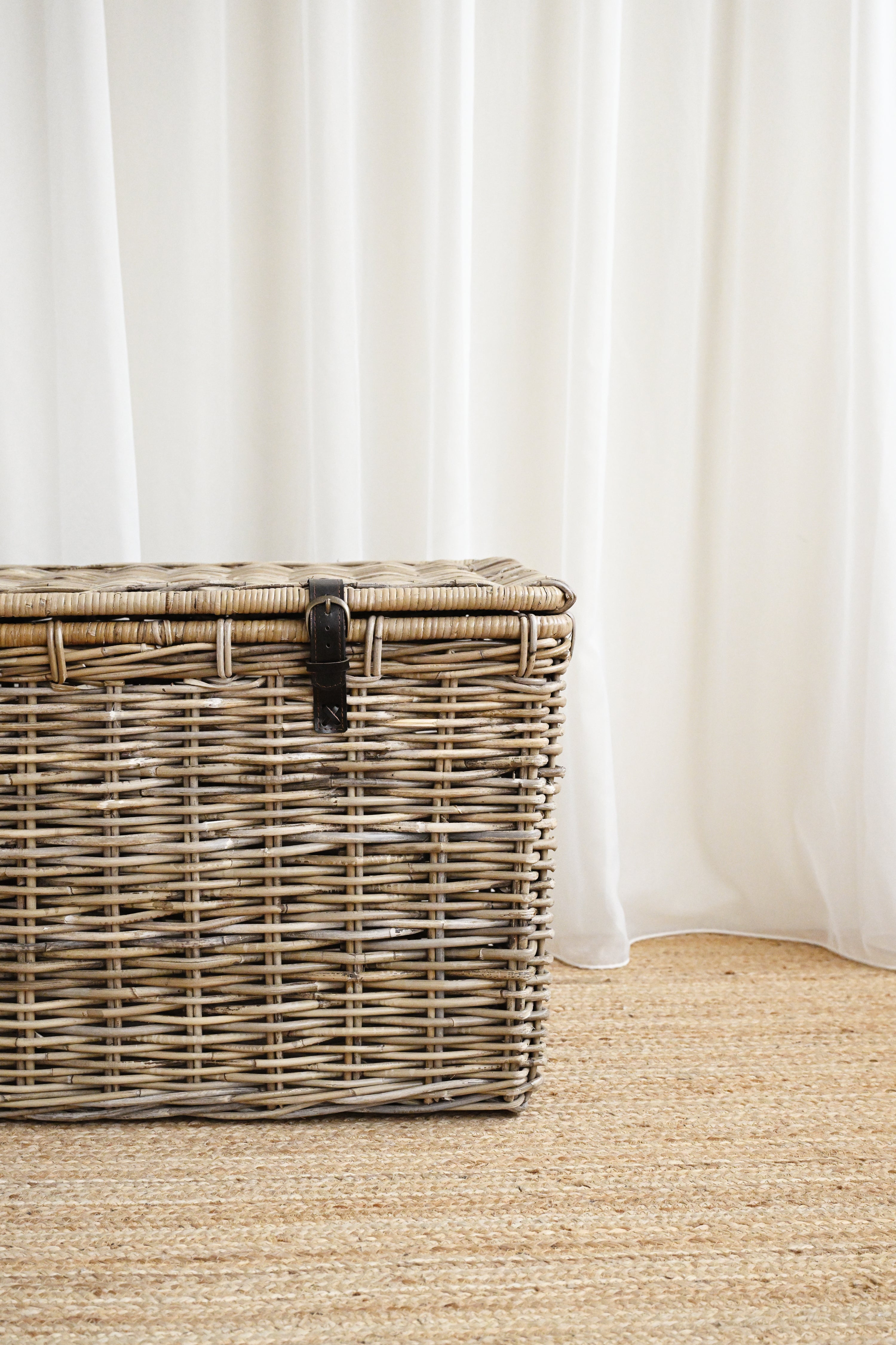 Wicker storage trunk on a beige carpet with white curtains in the background
