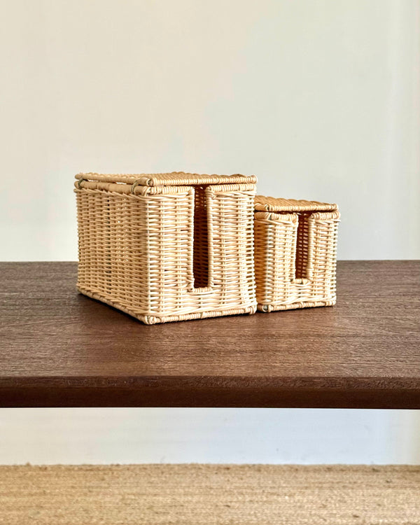 Two woven natural fiber storage baskets with cutout handles, displayed on a dark wood shelf against a light beige wall.
