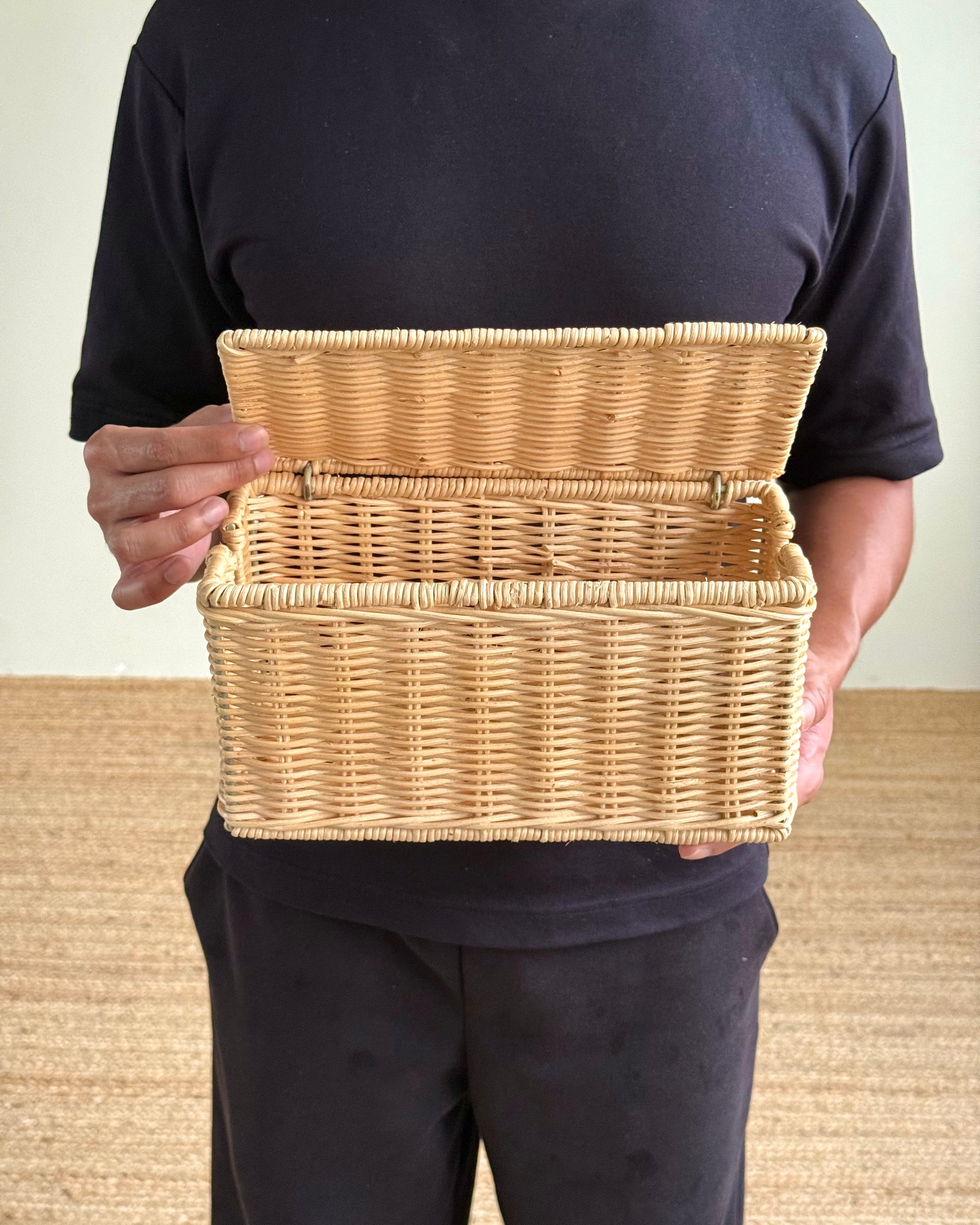 A person wearing a black t-shirt and black pants holds an open natural wicker storage basket against their torso.