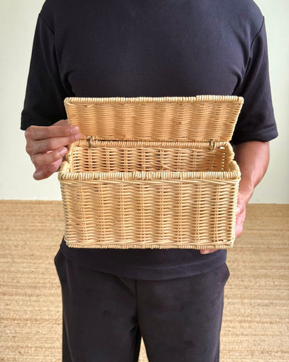 A person wearing a black t-shirt and black pants holds an open natural wicker storage basket against their torso.