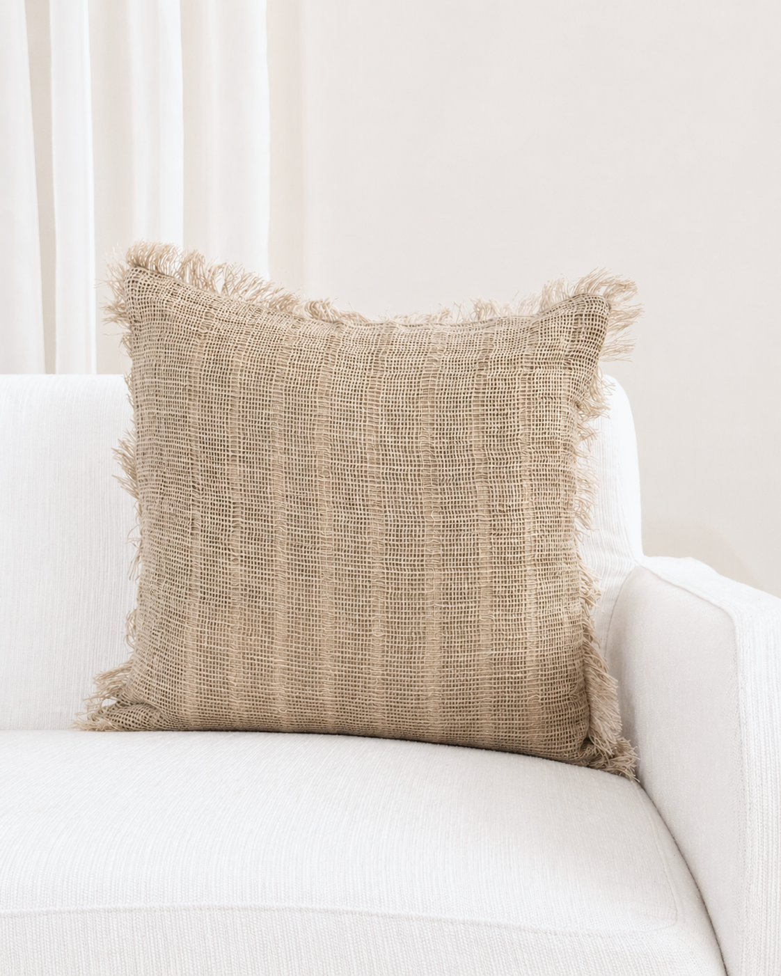Textured beige pillow with fringes on a white sofa