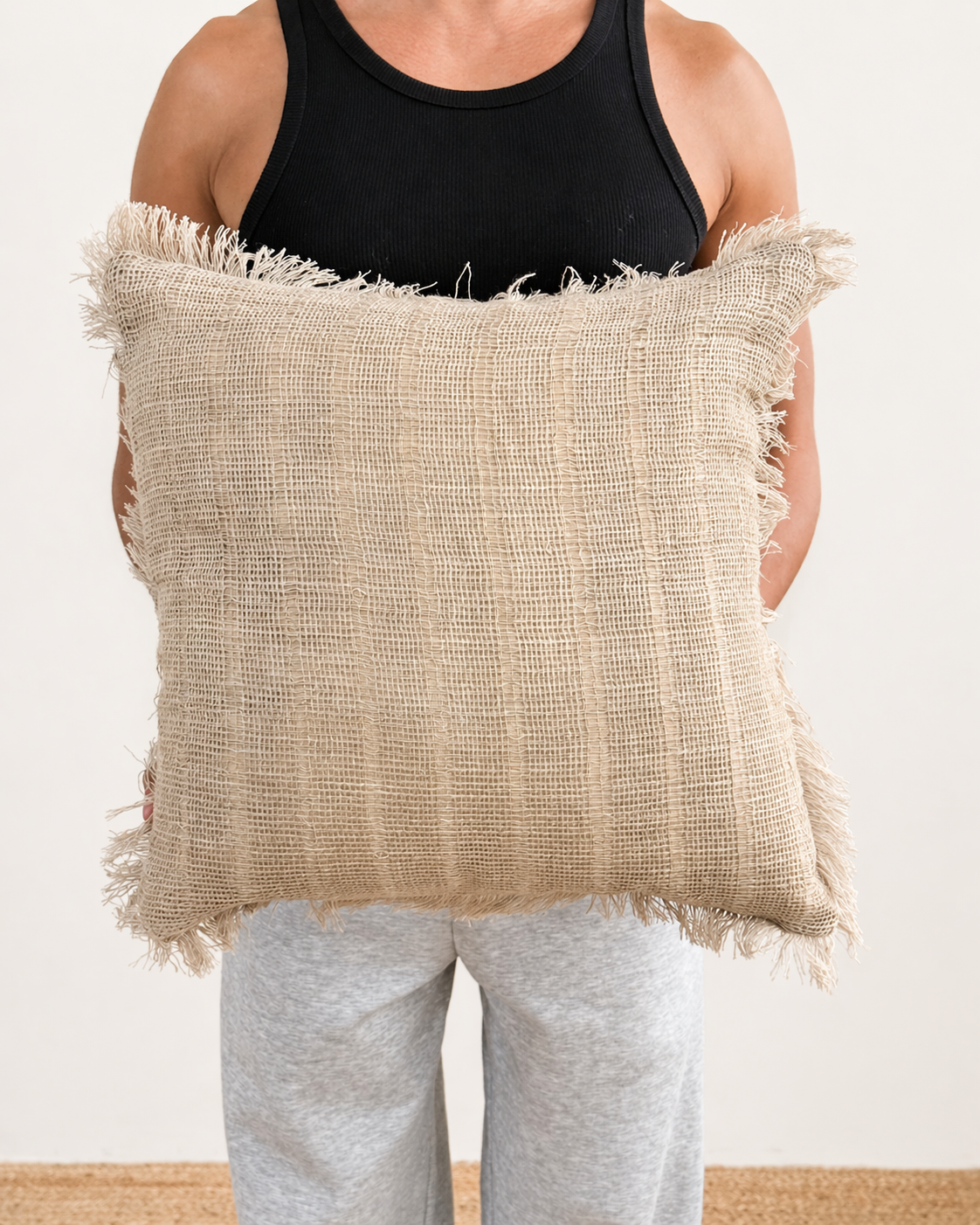 Person holding a textured beige pillow against a plain background