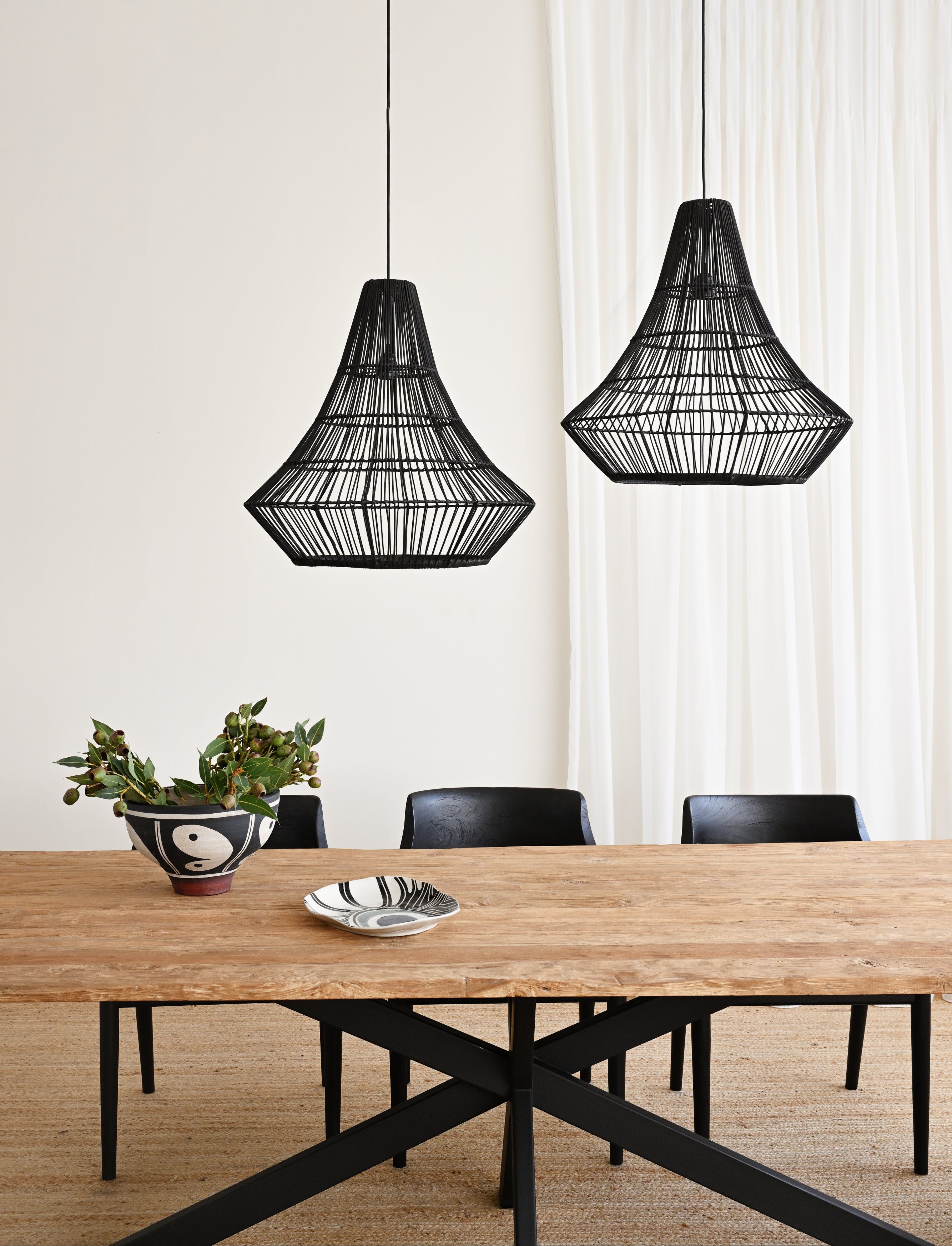 Two black woven pendant lights hanging above a wooden dining table with chairs.