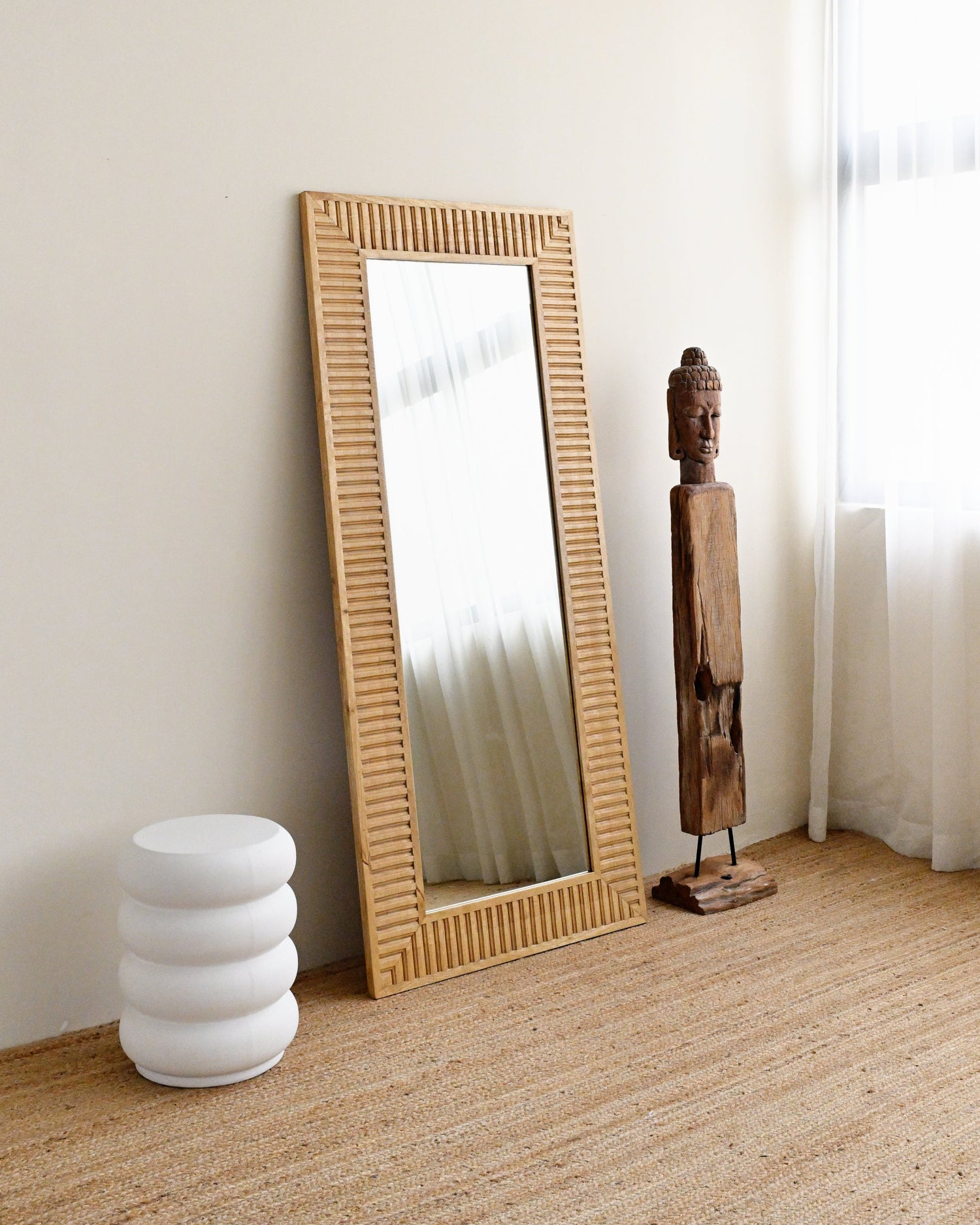 solid wood-framed mirror on a wooden floor with a white wall and curtain in the background