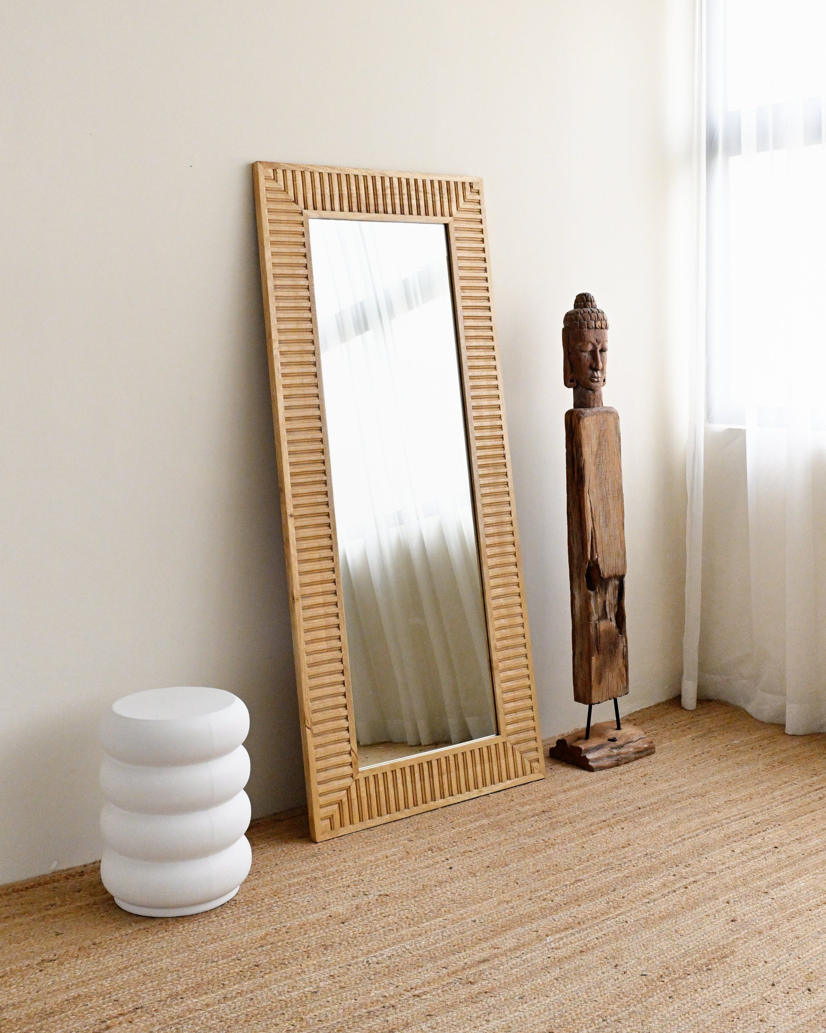 solid wood-framed mirror on a wooden floor with a white wall and curtain in the background