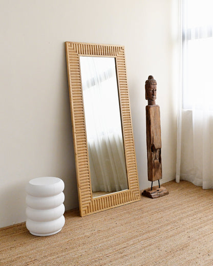 solid wood-framed mirror on a wooden floor with a white wall and curtain in the background