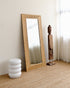 solid wood-framed mirror on a wooden floor with a white wall and curtain in the background