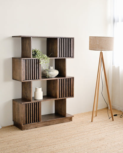 Wooden bookshelf with decorative items in a room with a lamp and white walls.