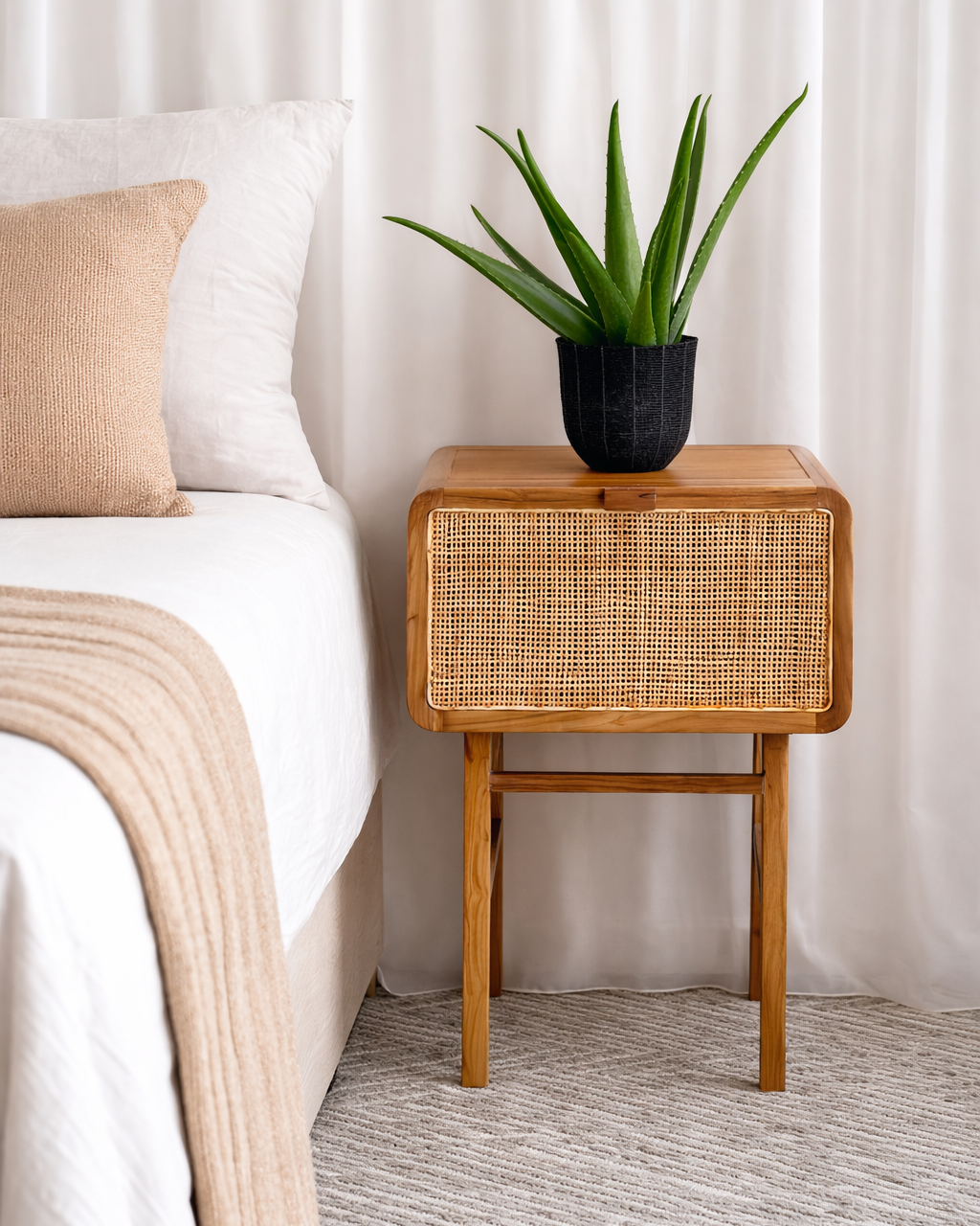 Wooden side table with a plant next to a bed in a bedroom setting