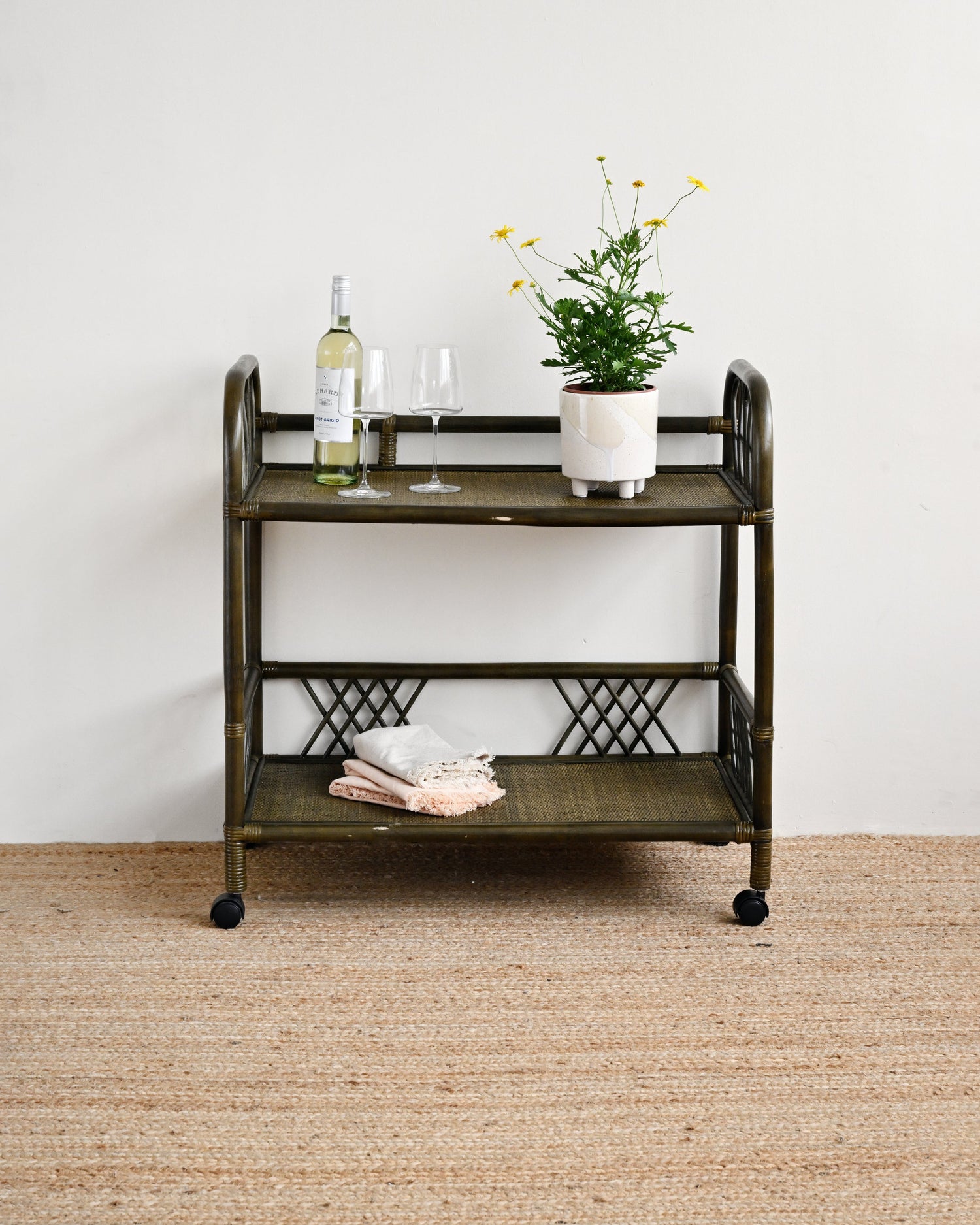 Vintage-style bar cart with a plant, bottle, and glasses on a neutral background