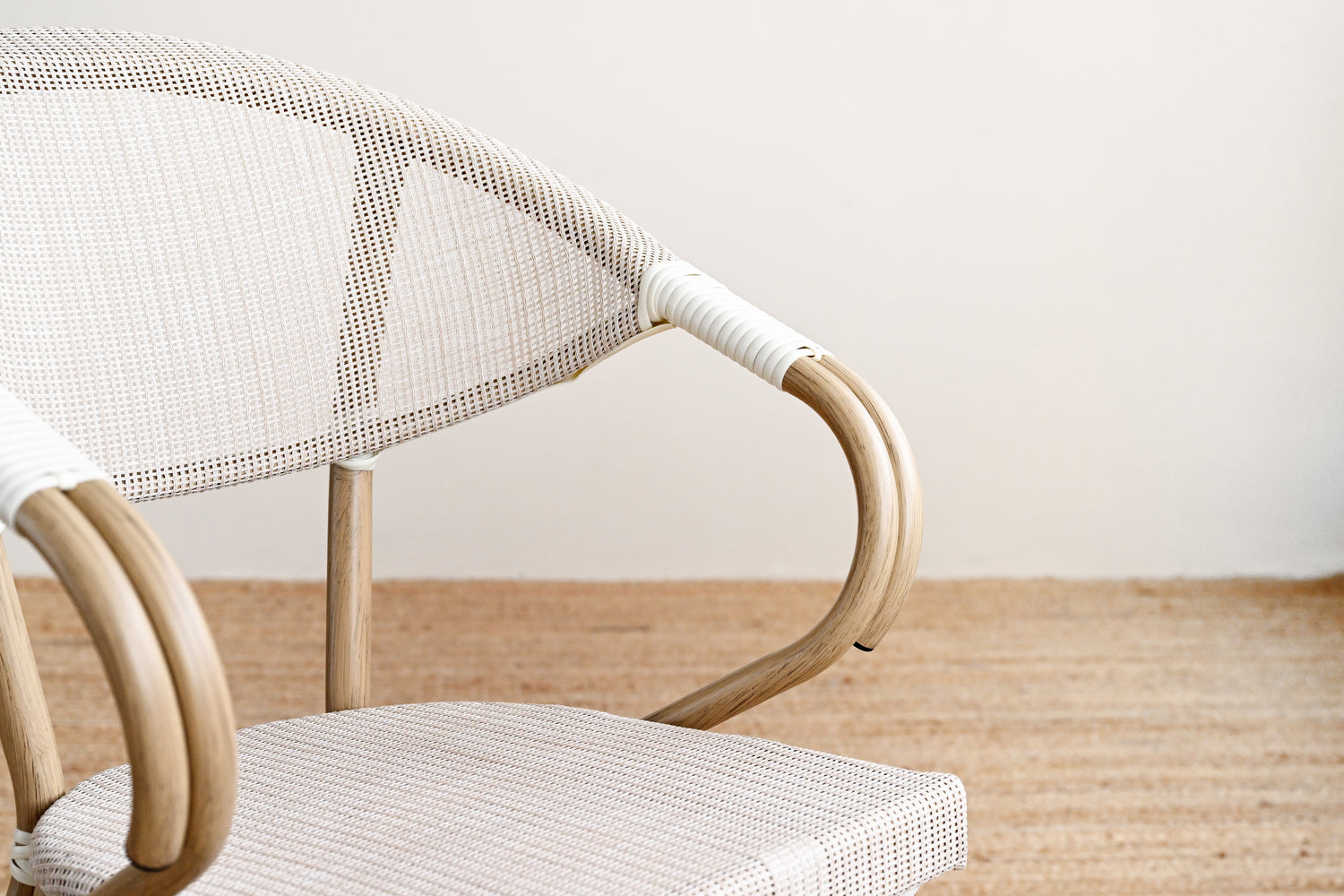 Close-up of a wicker chair with a white cushion on a wooden floor.