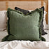 A green cushion cover with frayed edges on a bed, with other cushions in the background.